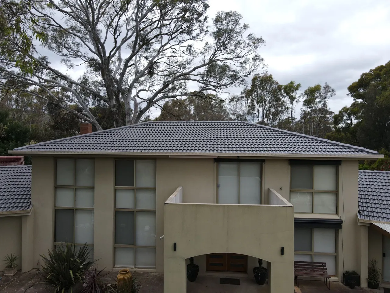 Concrete tile roof restored in charcoal grey on a two storey home framed by gum trees, recent client work in the Bendigo region