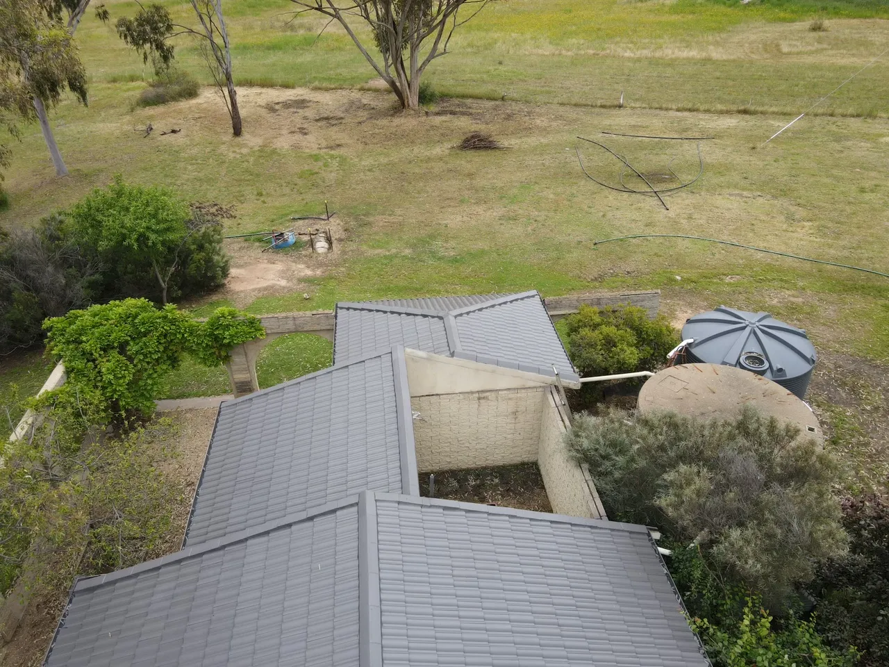 Rear wings and valleys Rear roof sections meeting at valleys, recoated in charcoal grey beside the water tanks on a rural block, tile roof restoration by Roof Restoration Services Bendigo